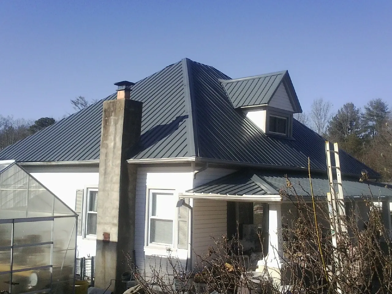 Dark blue standing seam metal roof on a white farmhouse with dormer — Slate & Tile Roof Repair by Roofing Brothers in Elbridge