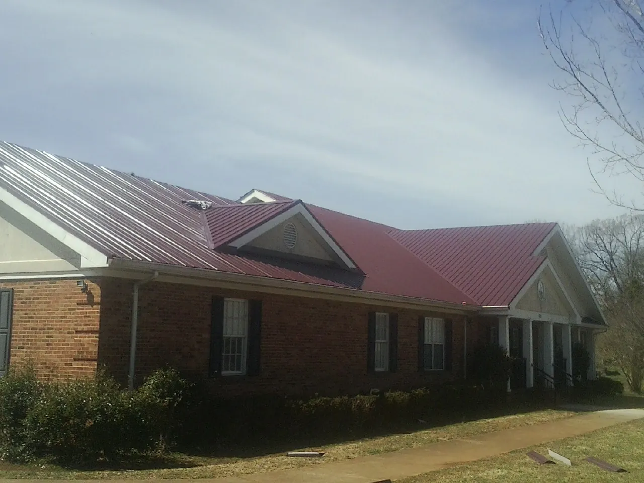 Red metal roof with gabled entries on a long brick building, from a Hail Damage Roof Repair job in Elbridge