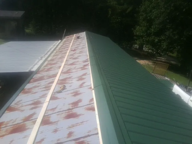 Old rusted panels beside newly installed green metal roofing — Wind Damage Roof Repair by Roofing Brothers in Elbridge