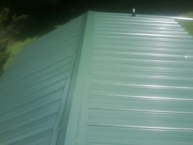 New green metal panels meeting at the ridge of a roof — Flat Roof Repair work by our crew in Elbridge