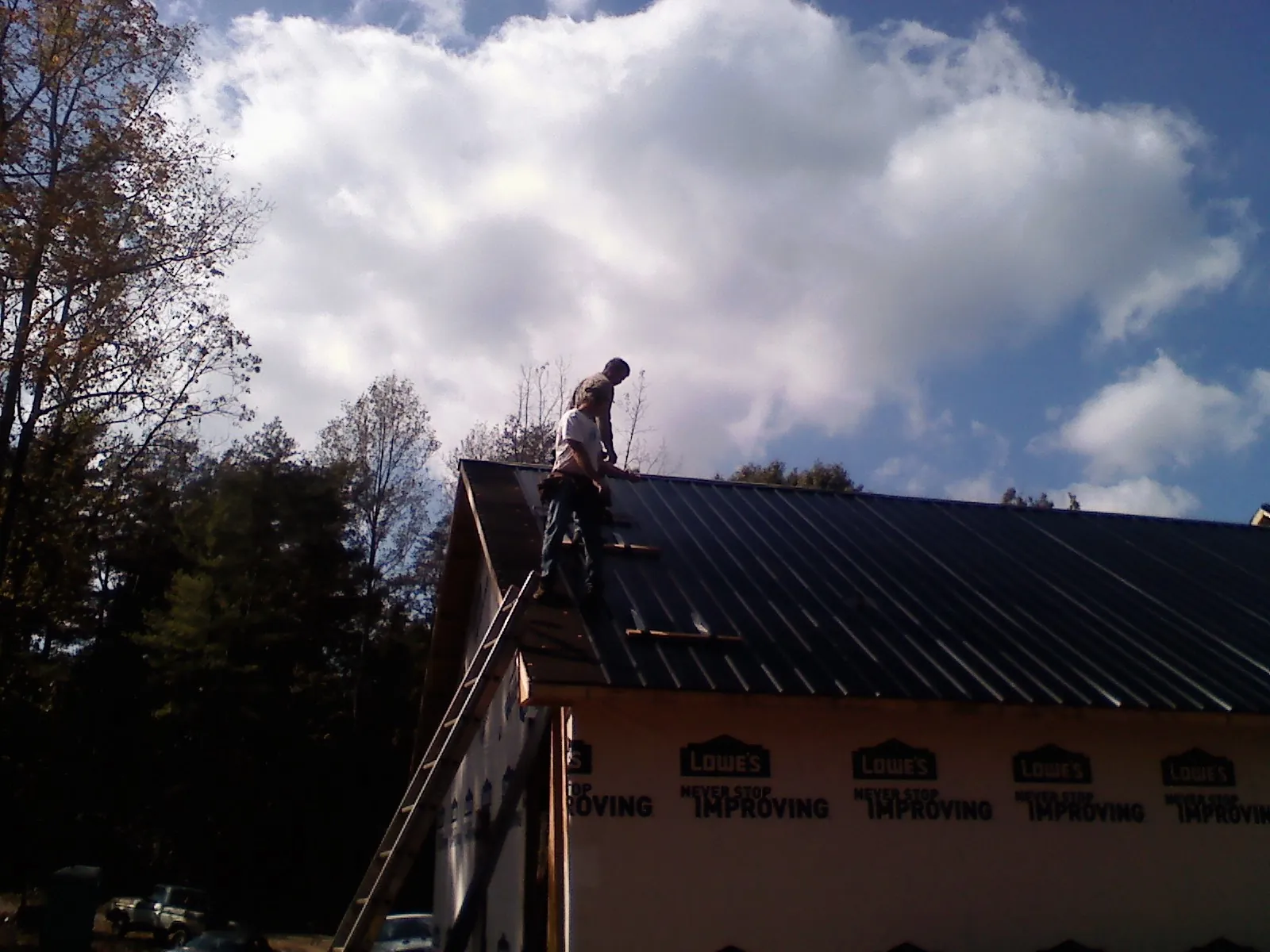 Roofer fastening dark metal panels high against a cloudy sky, from a Roof Inspection job in Elbridge