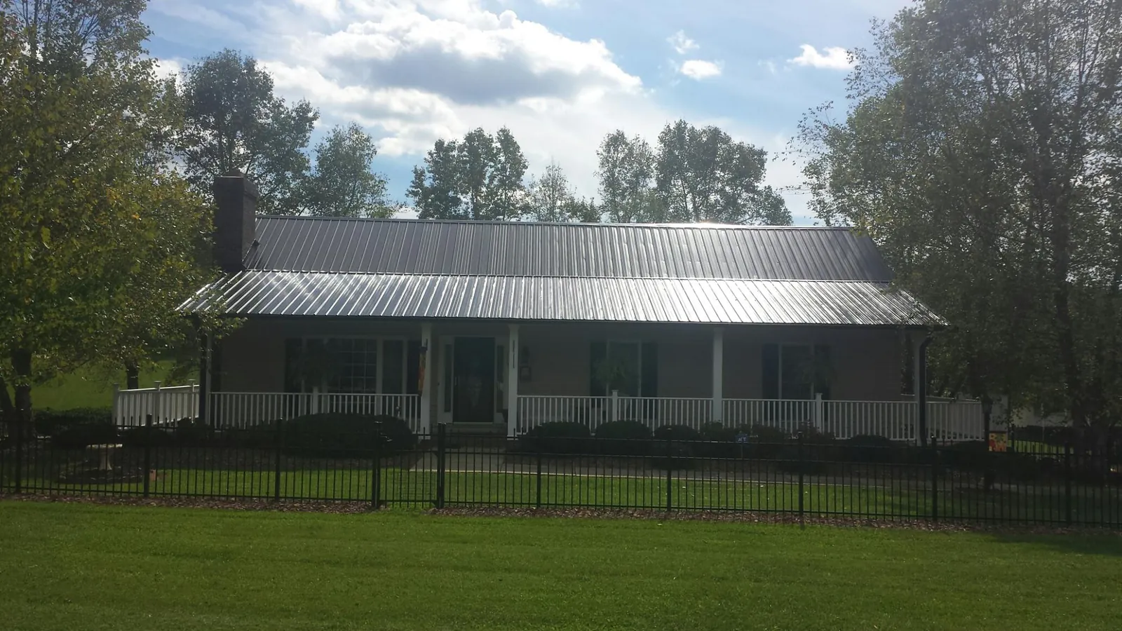 Gray metal roof on a brick ranch with a full width front porch — Gutter Guard Installation work by our crew in Elbridge