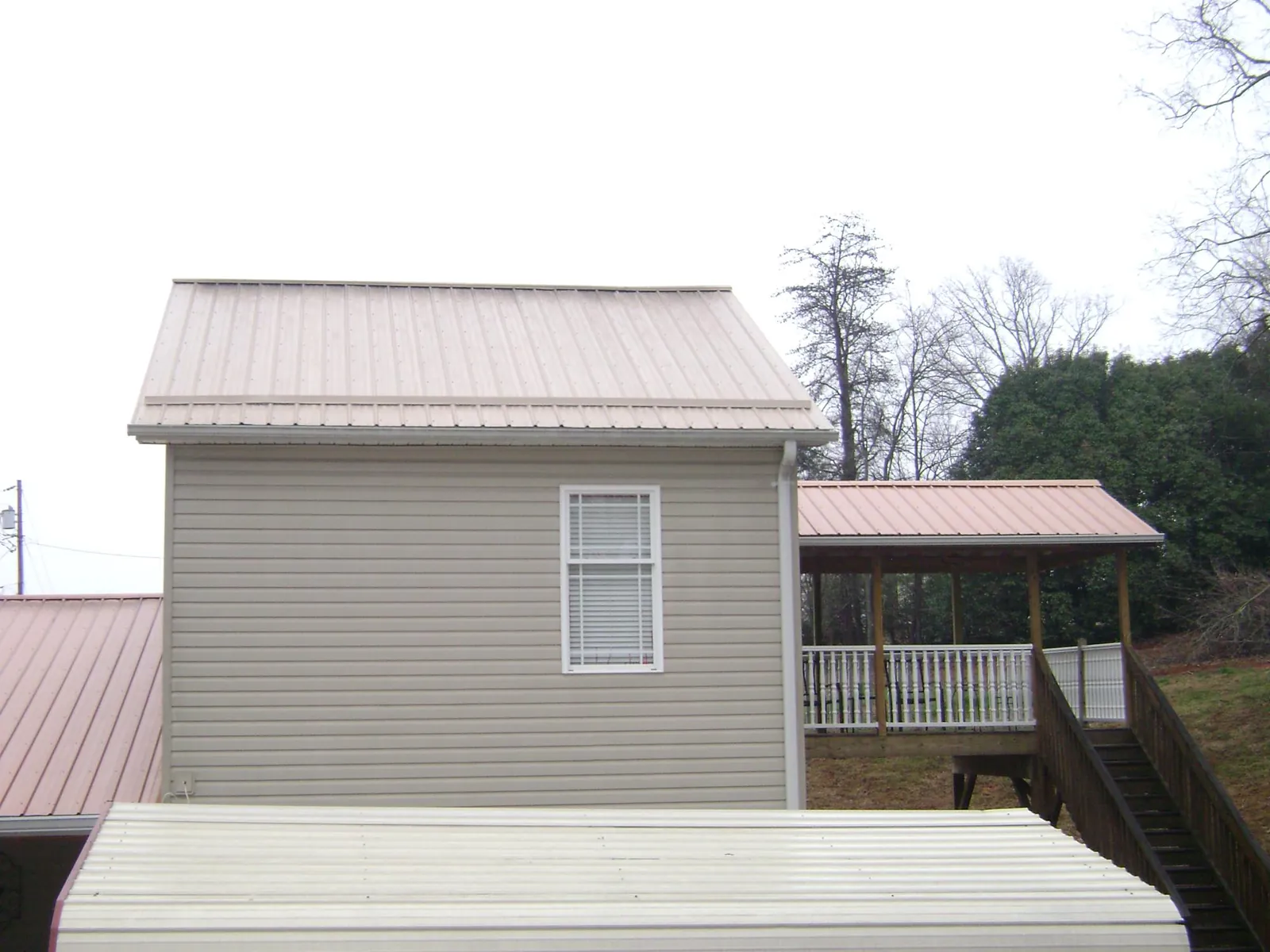 Tan metal roofs on a two story addition and attached porch, from a Roof Replacement job in Elbridge