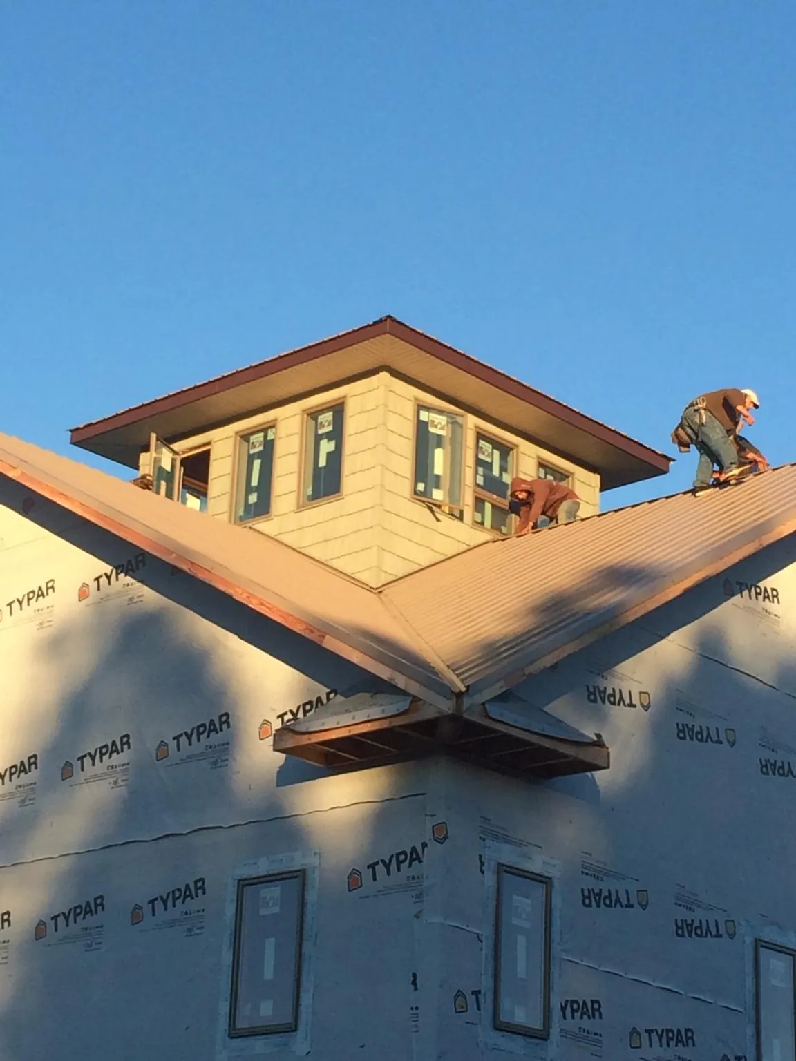 Roofers working around a rooftop cupola on a new metal roof at sunset — Roof Waterproofing in Elbridge by Roofing Brothers